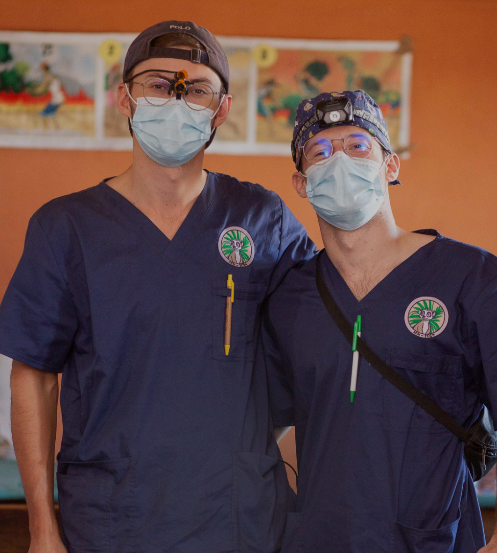 Two men in scrubs tops posing for picture while a volunteer trip
